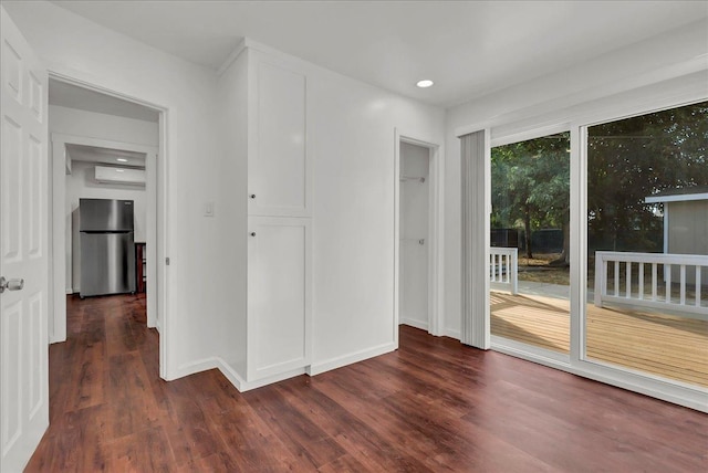 unfurnished bedroom with stainless steel refrigerator, dark wood-type flooring, access to exterior, and an AC wall unit