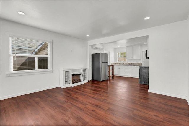 unfurnished living room with sink, an AC wall unit, and dark hardwood / wood-style floors