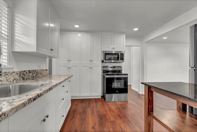 kitchen with dark hardwood / wood-style flooring, stainless steel appliances, white cabinetry, and light stone counters