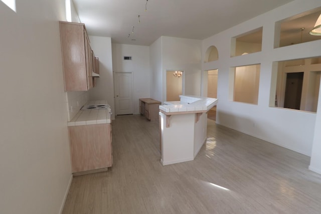 kitchen with light wood-type flooring, tile countertops, kitchen peninsula, and a breakfast bar