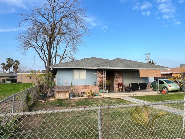 view of front of home with fence private yard, roof with shingles, a front lawn, and brick siding