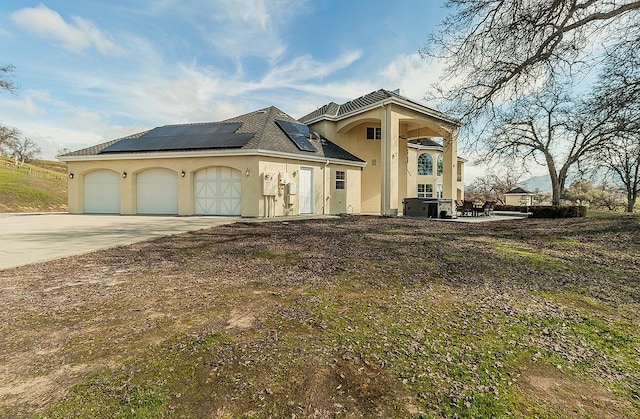 view of front of property featuring a garage, stucco siding, driveway, and solar panels