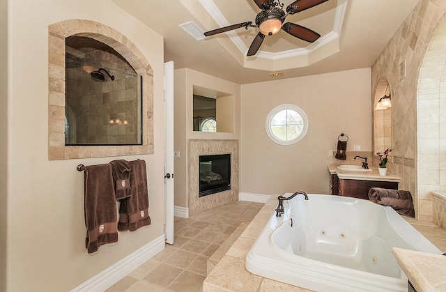 bathroom featuring vanity, ornamental molding, a whirlpool tub, a tiled fireplace, and a raised ceiling