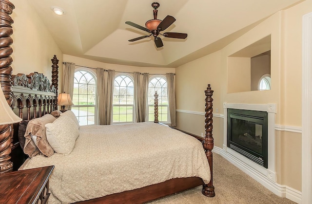 carpeted bedroom featuring a ceiling fan, a glass covered fireplace, baseboards, and a tray ceiling