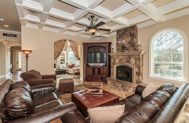 living area featuring arched walkways, coffered ceiling, ornamental molding, beamed ceiling, and a stone fireplace