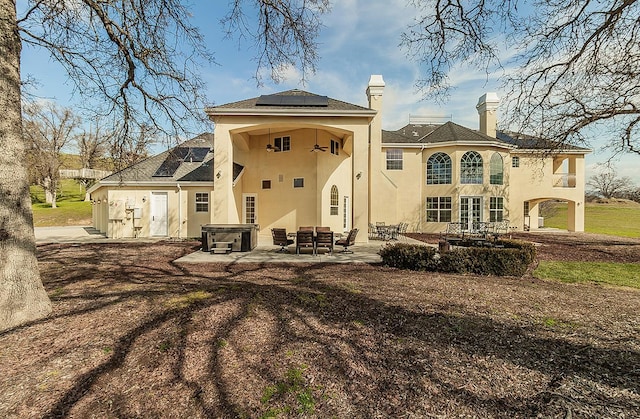 back of property with a patio area, roof mounted solar panels, a chimney, and stucco siding