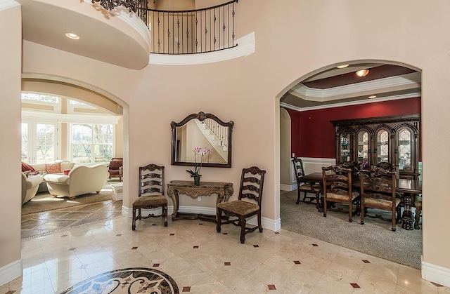 interior space with baseboards, arched walkways, a high ceiling, crown molding, and carpet flooring