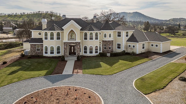 french country inspired facade featuring stone siding, a front yard, a mountain view, and stucco siding