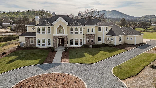 french country inspired facade featuring stone siding, a front yard, a mountain view, and stucco siding