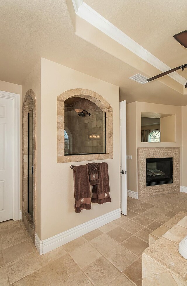 bathroom with visible vents, a fireplace, a tile shower, and baseboards