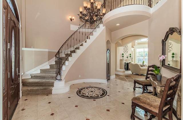 foyer entrance with baseboards, arched walkways, stairway, a high ceiling, and a notable chandelier