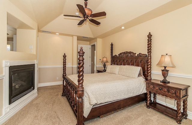 bedroom with visible vents, vaulted ceiling, a glass covered fireplace, and light colored carpet