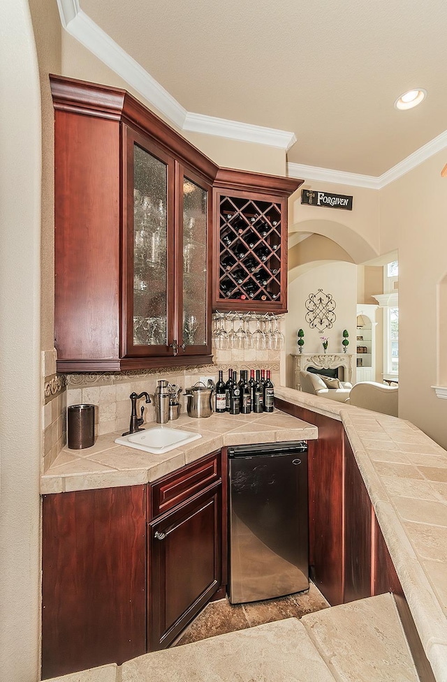 bar with a sink, ornamental molding, fridge, backsplash, and indoor wet bar