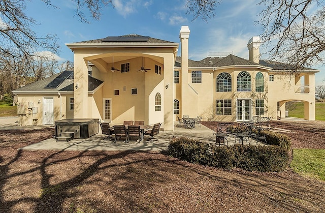 back of property featuring outdoor dining area, a patio, a hot tub, and solar panels