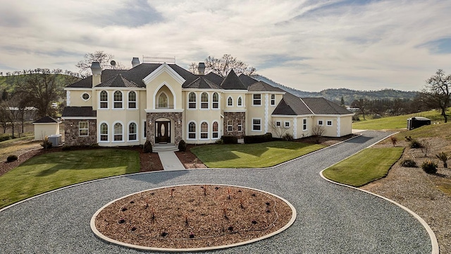 french provincial home with curved driveway, a chimney, central air condition unit, stone siding, and a front lawn