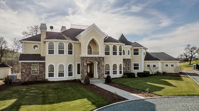 view of front of house with a chimney, a front yard, central AC, a balcony, and stone siding