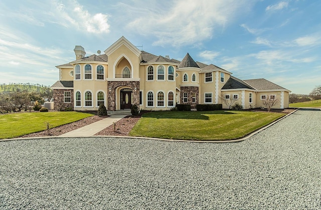 french provincial home featuring stone siding, a chimney, a front lawn, and stucco siding