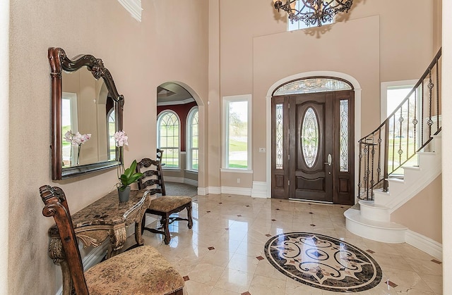 foyer entrance featuring arched walkways, a high ceiling, stairs, and baseboards