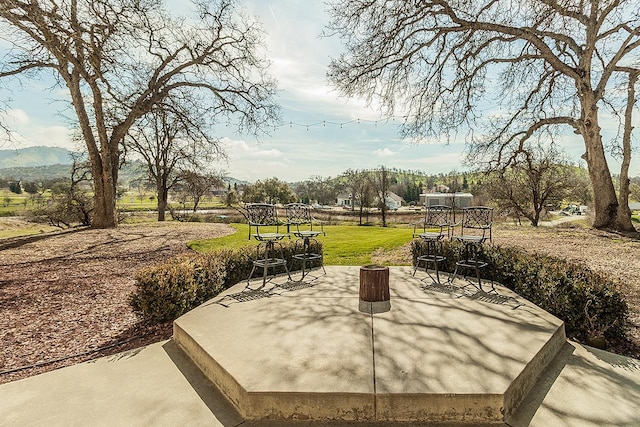 view of property's community with a mountain view, outdoor dining area, a lawn, and a patio