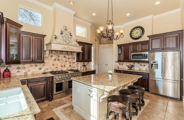 14505 Blue Drake Ln, Prather, CA 93651 - kitchen featuring appliances with stainless steel finishes, light stone countertops, ornamental molding, dark brown cabinetry, and a center island