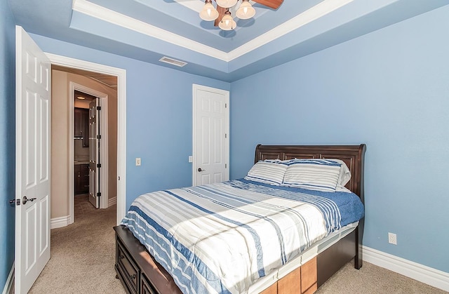 bedroom with light carpet, visible vents, a tray ceiling, and baseboards