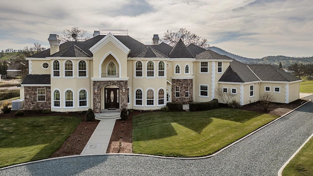 view of front of home with a chimney, stucco siding, a front yard, cooling unit, and stone siding