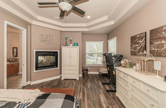 bedroom featuring dark wood-style floors, a tray ceiling, a multi sided fireplace, and baseboards