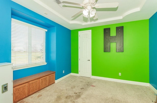 empty room with baseboards, a raised ceiling, and light colored carpet