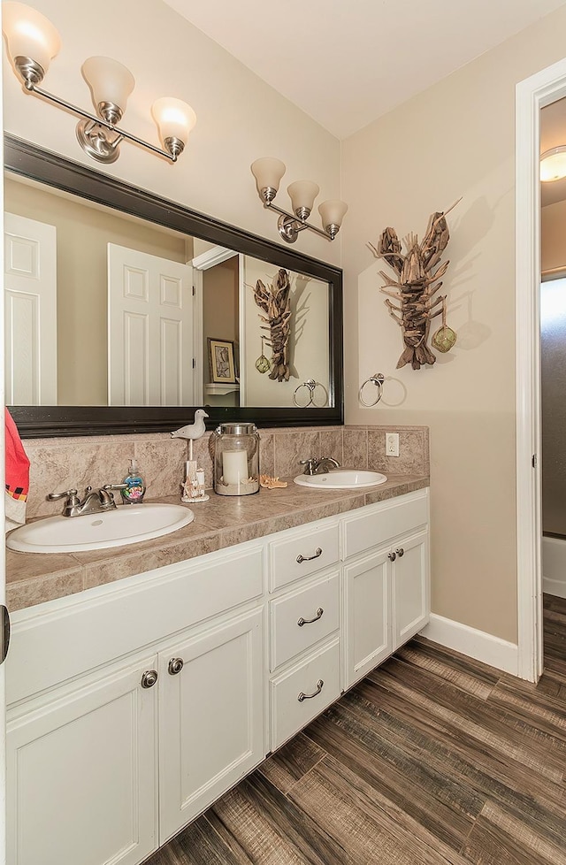 bathroom featuring wood finished floors, a sink, baseboards, and double vanity