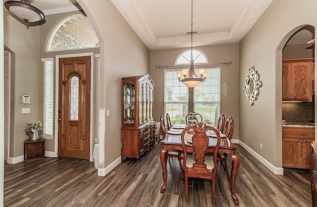 dining area with a tray ceiling, dark wood finished floors, and arched walkways