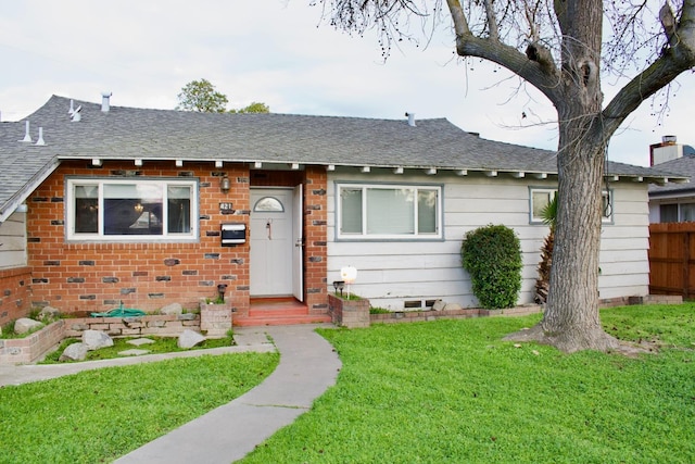 view of front of house featuring a front lawn, crawl space, a shingled roof, brick siding, and fence