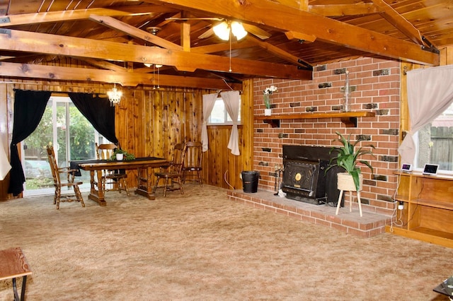 carpeted living area featuring a wood stove, ceiling fan, vaulted ceiling with beams, wood walls, and wood ceiling