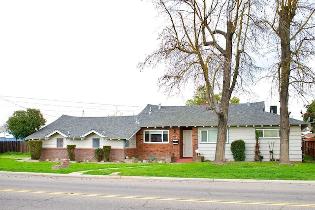 ranch-style house with a shingled roof, a front yard, and fence