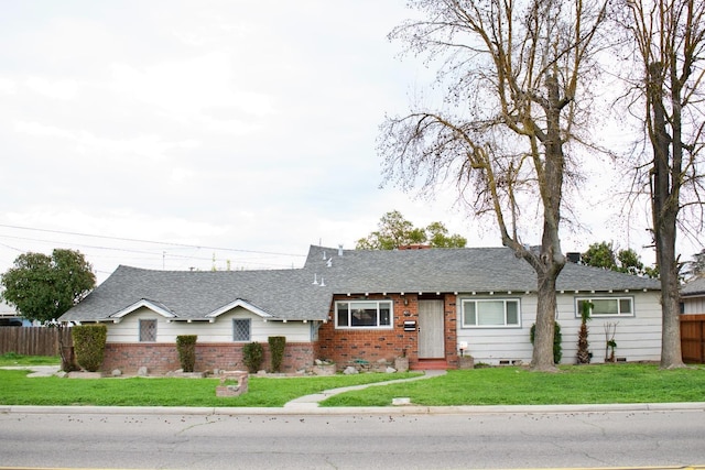 ranch-style home featuring brick siding, fence, a shingled roof, and a front yard
