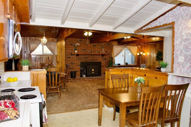 dining space with a wood stove, beamed ceiling, wallpapered walls, and carpet