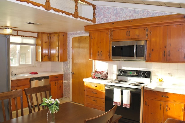 kitchen with tasteful backsplash, stainless steel appliances, brown cabinetry, and tile countertops