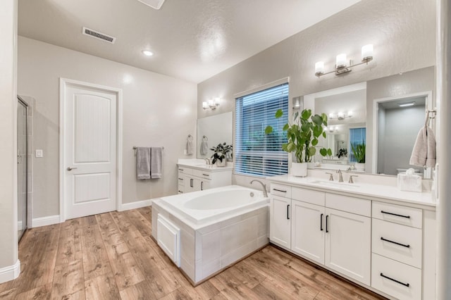 bathroom featuring wood finished floors, two vanities, a sink, and visible vents