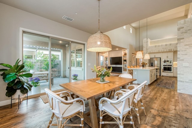 dining space featuring light wood-style flooring, a high ceiling, visible vents, and baseboards