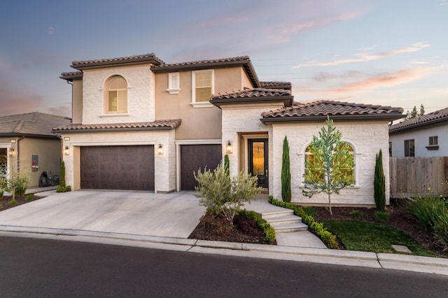 mediterranean / spanish house featuring stucco siding, an attached garage, fence, driveway, and a tiled roof