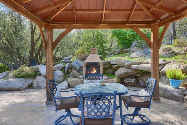 view of patio / terrace with a gazebo, outdoor dining area, and a warm lit fireplace