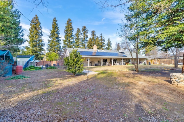 back of house with a fenced backyard, solar panels, and a chimney