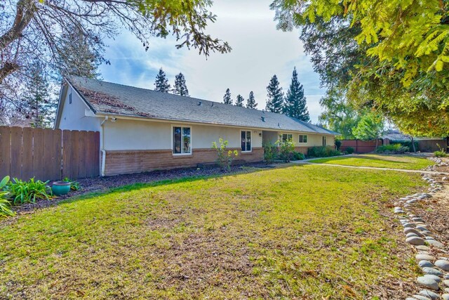 back of property featuring brick siding, fence, a lawn, and stucco siding