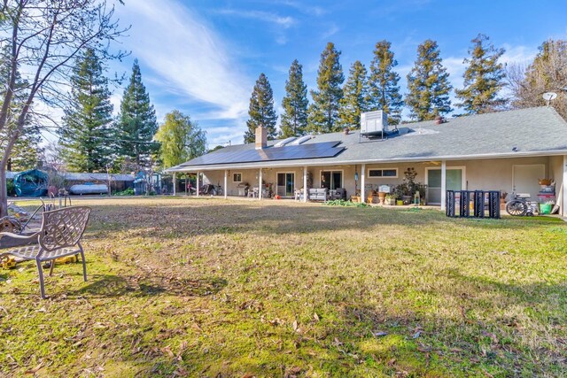 rear view of house featuring stucco siding, a lawn, a chimney, and solar panels