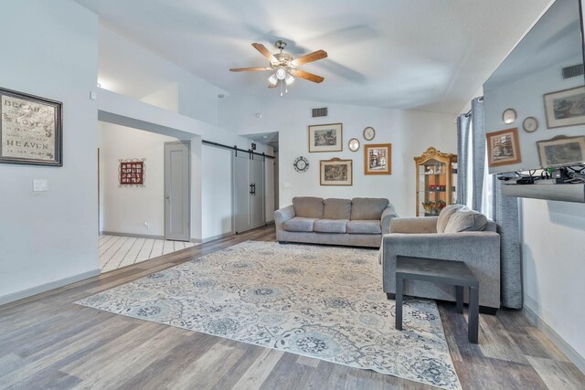 living room featuring a barn door, visible vents, lofted ceiling, ceiling fan, and wood finished floors