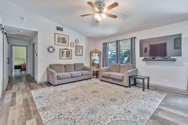 living area with lofted ceiling, a barn door, ceiling fan, and wood finished floors