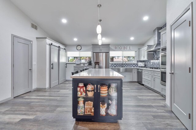 kitchen featuring a barn door, a kitchen island, light countertops, stainless steel appliances, and pendant lighting