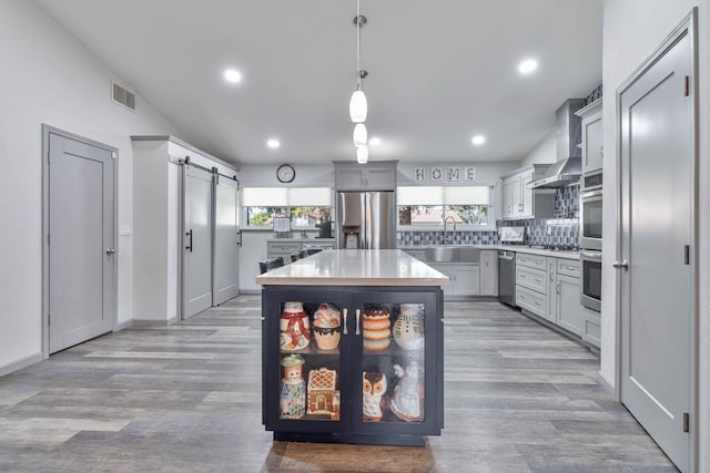 kitchen featuring light countertops, wood finished floors, stainless steel appliances, visible vents, and wall chimney exhaust hood