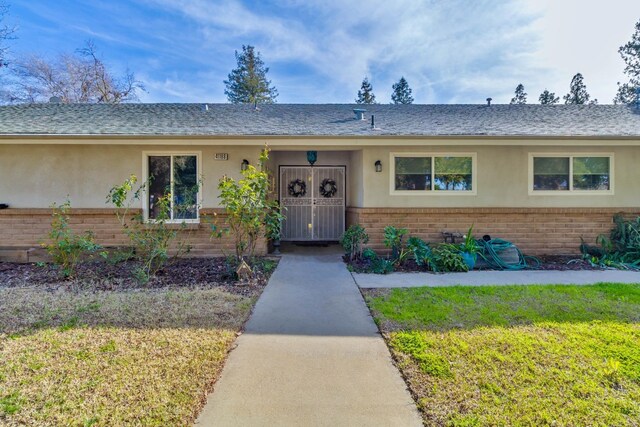 ranch-style house featuring roof with shingles, brick siding, a front lawn, and stucco siding