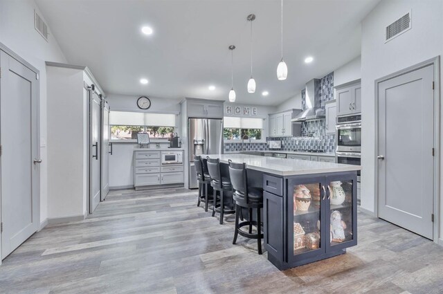 kitchen featuring pendant lighting, a breakfast bar area, light countertops, a kitchen island, and wall chimney exhaust hood