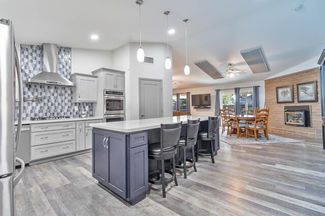 kitchen featuring hanging light fixtures, wall chimney exhaust hood, open floor plan, and light countertops